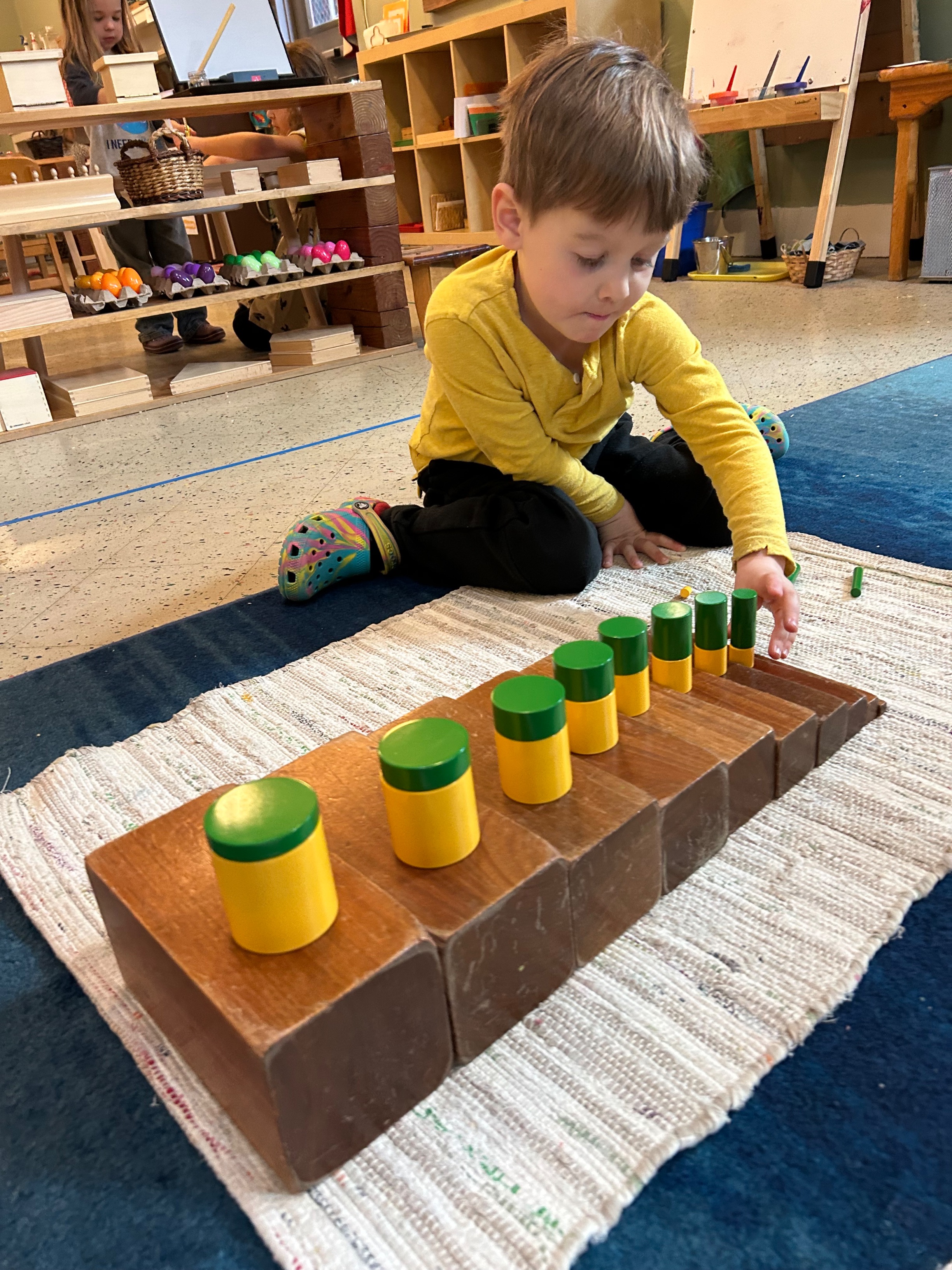 Preschool-aged boy on the floor using the brown stair and knobless cylinders.