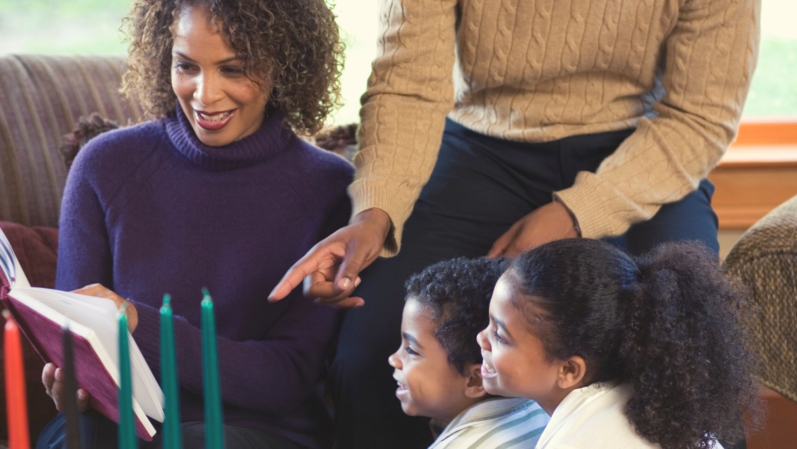 A family of four looking at a book together. There are Kwanzaa candles in the foreground.