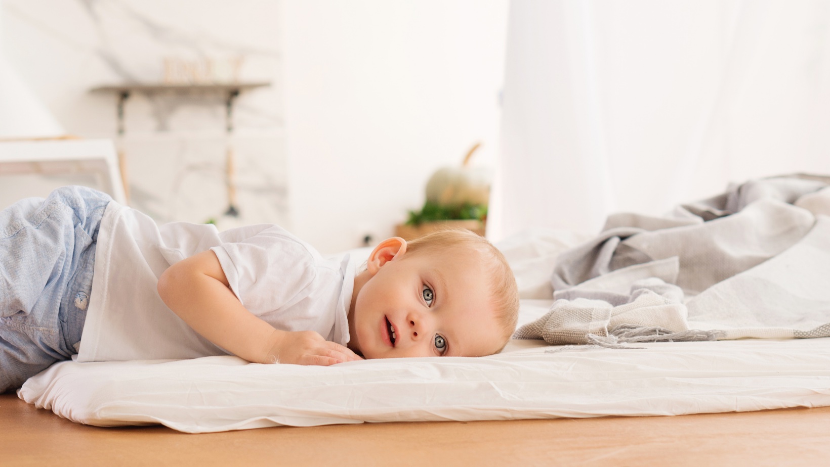Baby lying on sleeping mat on floor, awake.