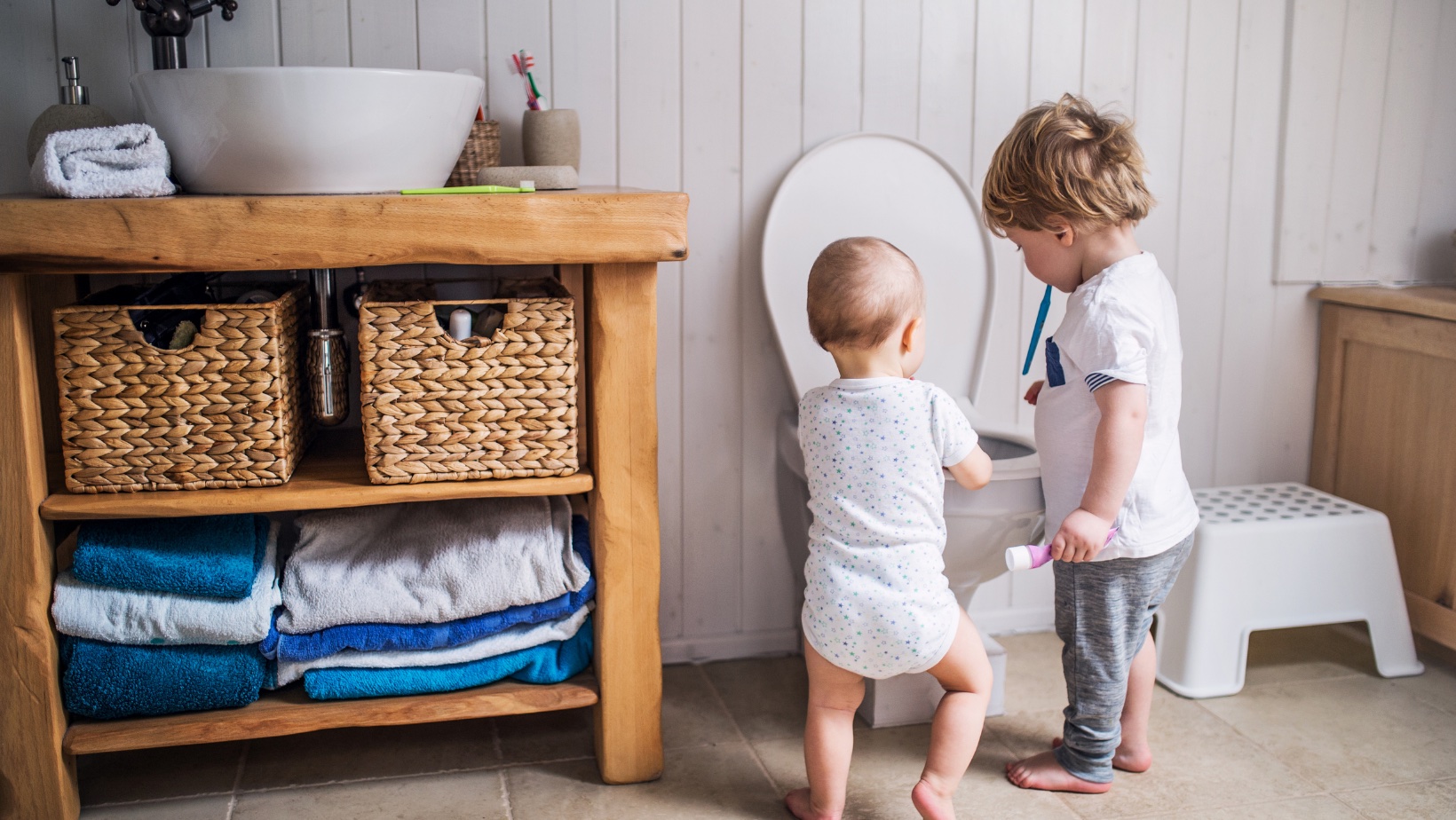 Two toddlers in bathroom examining a toilet.