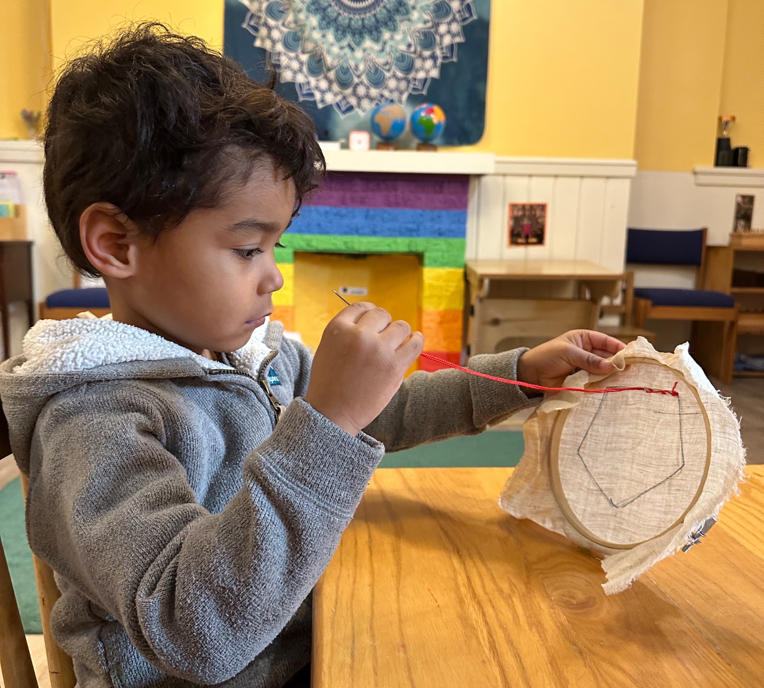 Preschool-aged boy sewing over the outline of a pentagon