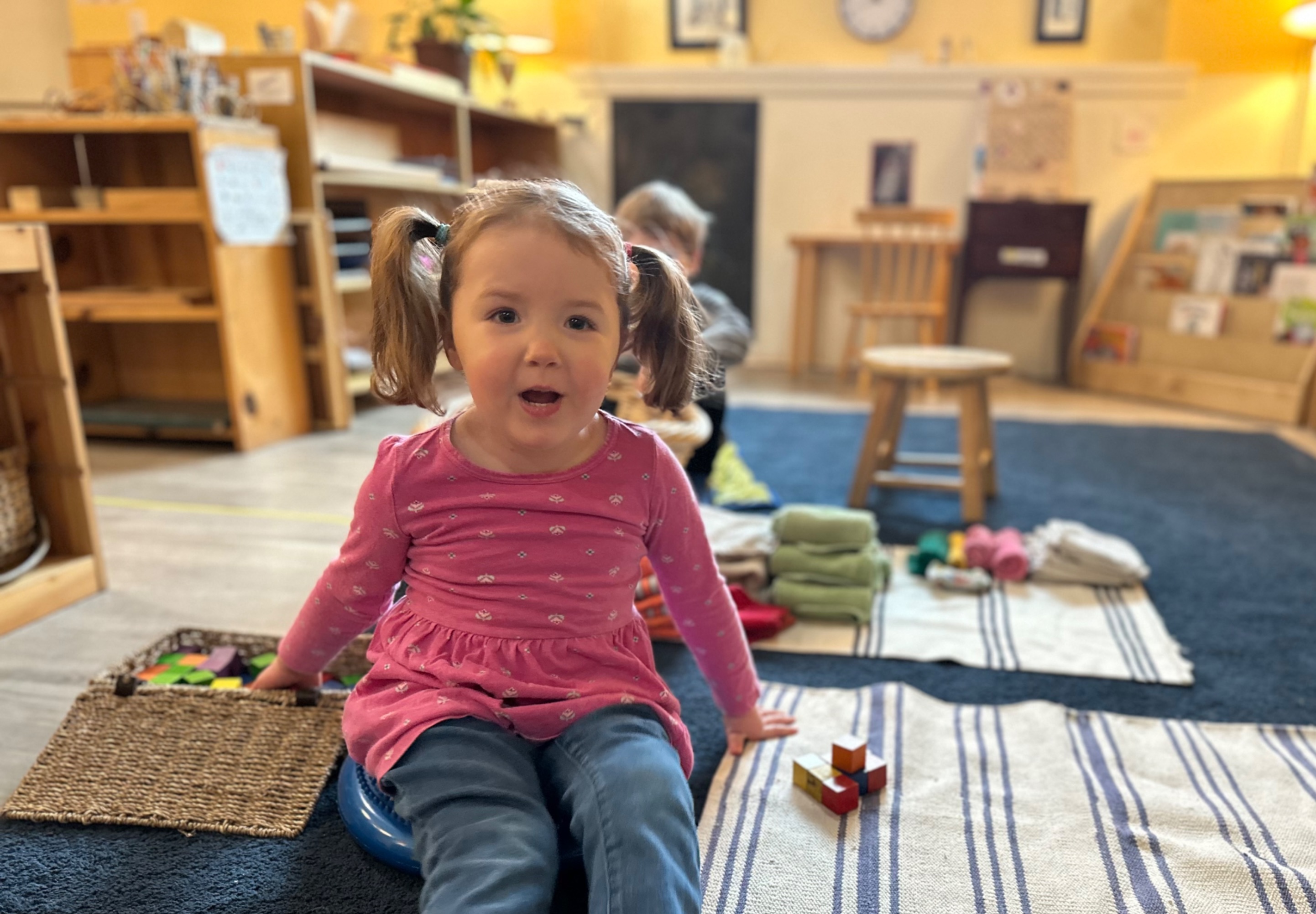 Preschool-aged girl sitting on floor near blocks, looking at camera and smiling
