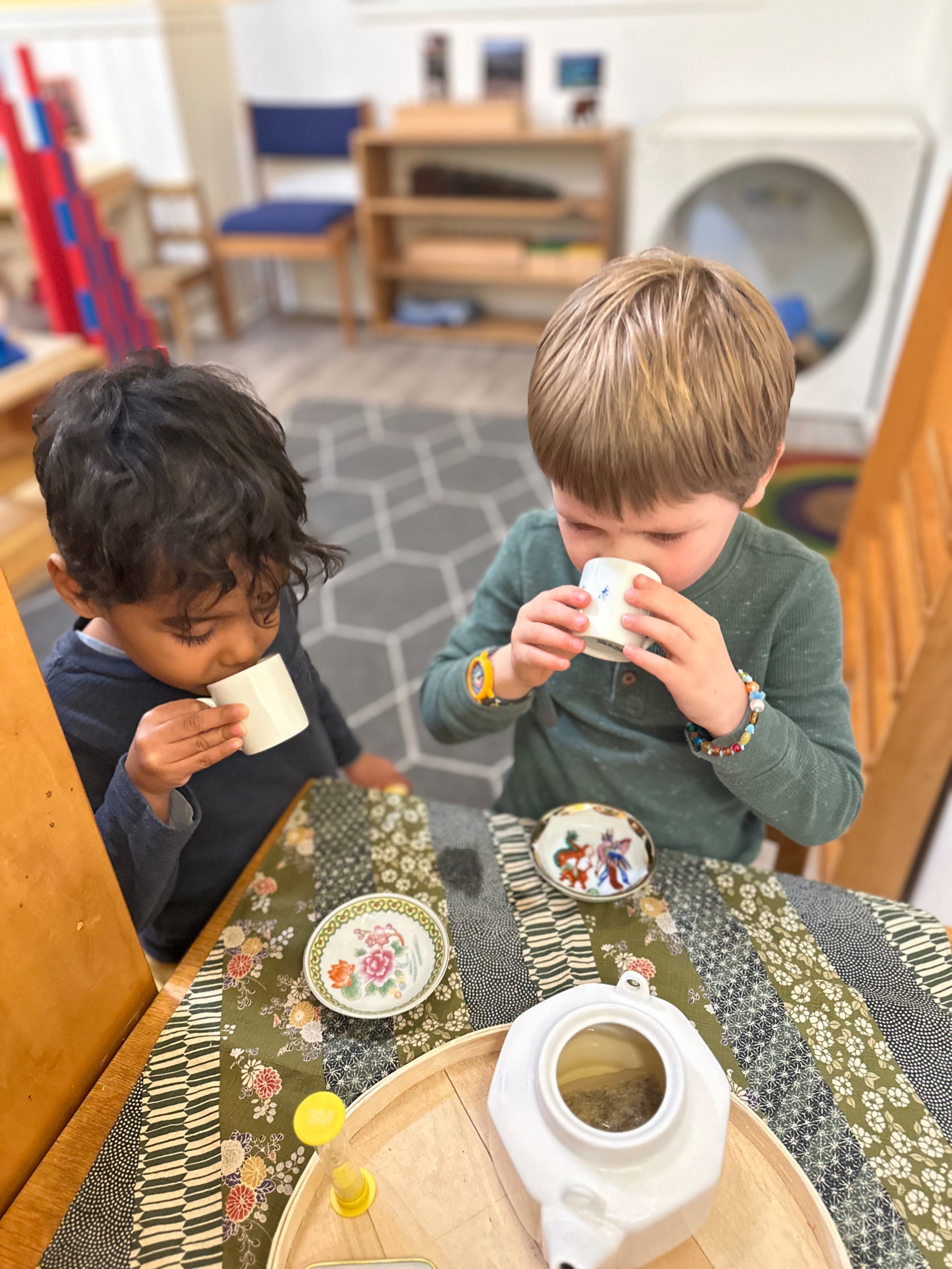 Two preschool-aged boys seated at a table sipping tea.