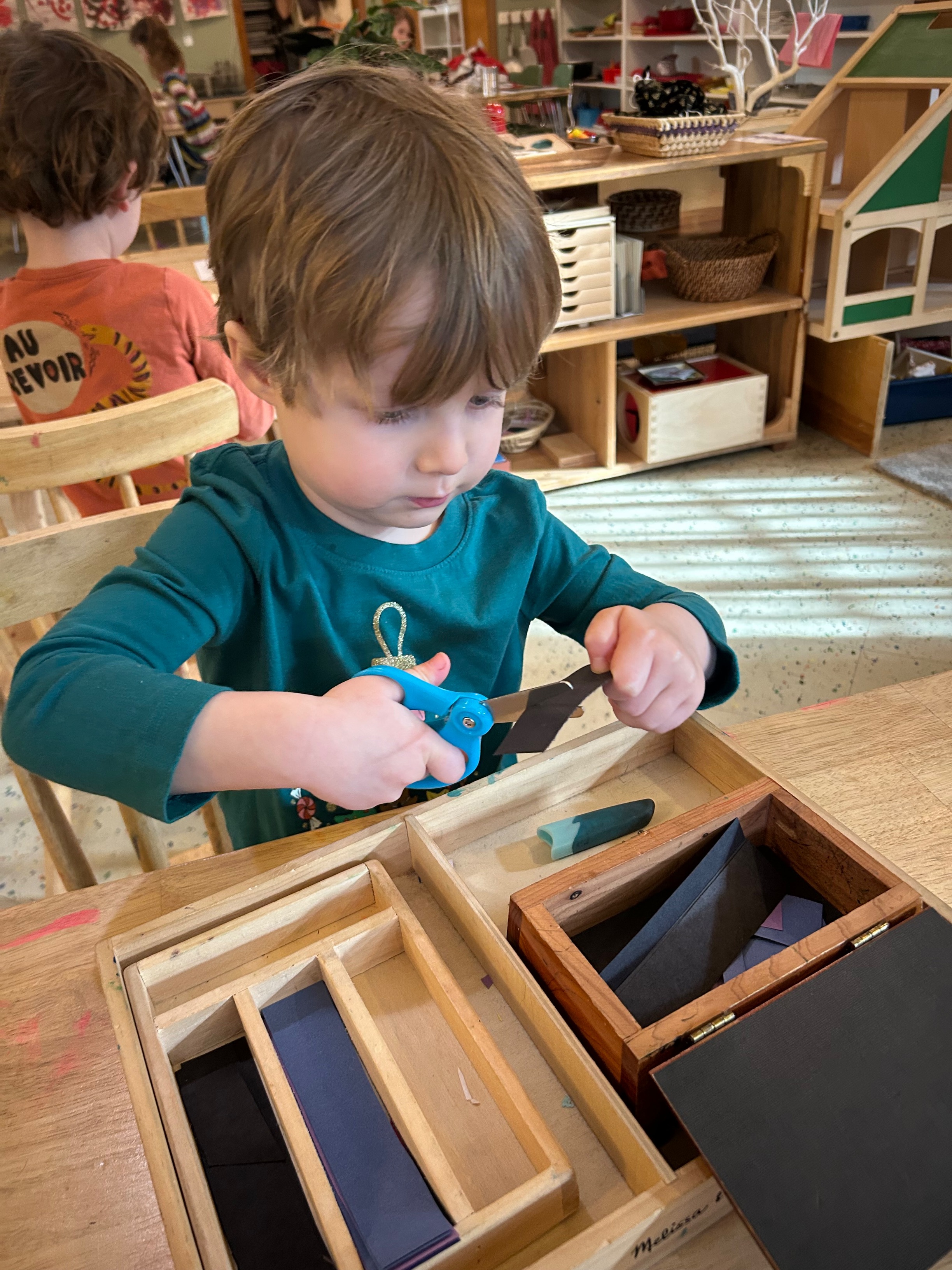A preschool-aged boy seated at a table cutting strips of paper with scissors.